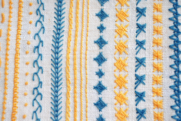 Different examples of yellow and blue patterns of embroidery on white fabric