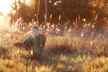 Young boy, shoot with handmade bow and arrow at target on sunset, summertime outdoors.