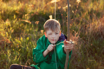 YPortrait young boy, shoot with handmade bow and arrow at target on sunset, summertime outdoors.