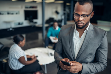 Portrait of a confident black businessman looking down on his mobile phone and all african team in the background