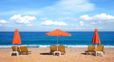 Abstract image with sun loungers and orange umbrellas from the sun on the beach on the seafront with waves (relaxation, harmony, holidays - concept)