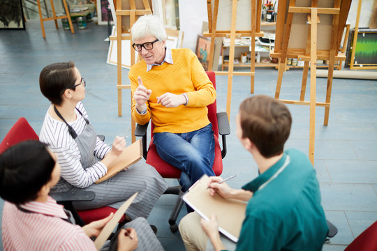 High angle portrait of mature art teacher talking to group of students sitting in circle in art studio