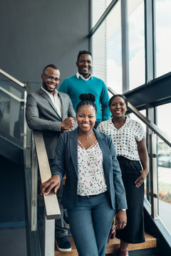 Team of african business people smiling and standing on stairs in a modern office