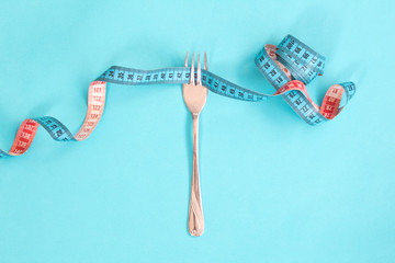 Tape measure around a fork as concept for diet. Fork are wrapped in blue measuring tape on blue background. 