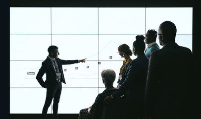 Indian businessman pointing at digital screen during a presentation with team of people watching