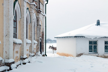 A drawn horse stands between buildings in the winter on a snowy town street. Veliky Ustyug, Russia.