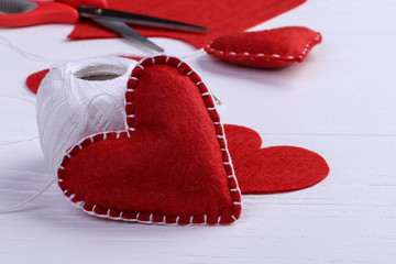 Handmade red felt heart next to threads and a needle on a white table. Women's Day Concept, Copy Space.