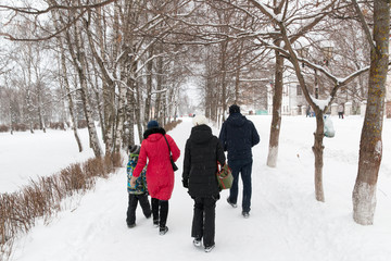 Fototapeta na wymiar Back view to the family that walks along the winter alley among the snow-covered trees
