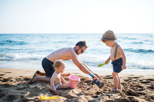 A father with two toddler children playing with sand on beach on summer holiday.