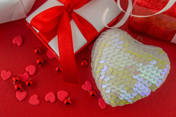 Valentines day concept. White heart and gift boxes with red decorative tape and tiny hearts on a red background. Close up. Top view.