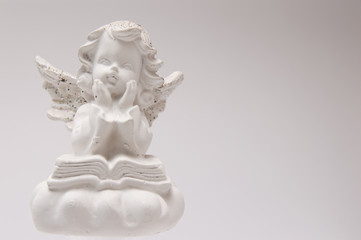 Fototapeta na wymiar gypsum white angel on a white background reading a book and thinking
