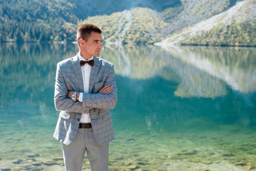 Handsome groom in wedding suit standing near the lake in the mountains. Morskie Oko