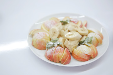 Dish with sliced ​​apple and banana and powdered sugar. Healthy dessert on white background