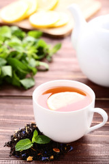 Cup of tea with mint leafs and teapot on brown wooden table
