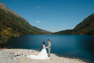 Wedding couple of groom and bride standing on the lake shore in Tatra mountains. Morskie Oko, Poland