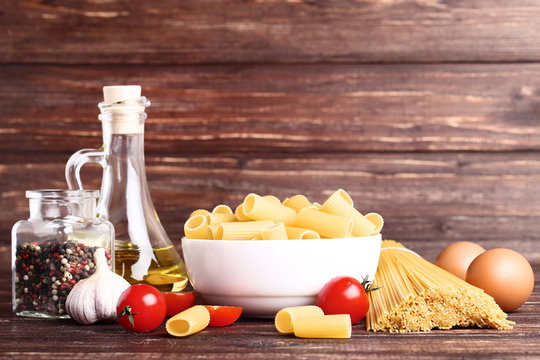 Different Pasta With Tomatoes, Garlic And Papper On Brown Wooden Table