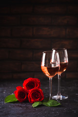 Two wine glasses of rose wine on brick background, bouquet of red roses for romantic evening for Valentines day surprise, marriage proposal passion and love celebration, copy space 