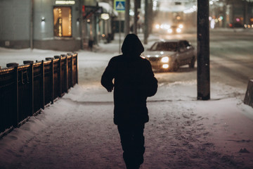 Silhouette of a man in the hood that walks down the street at night in the snowfall