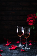 Two wine glasses of rose wine on brick background, bouquet of red roses for romantic evening for...