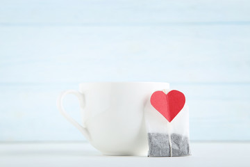 White cup with teabag and red heart on wooden table