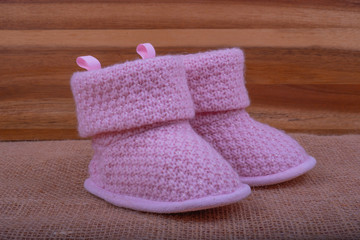 Baby infant pink knitted boots on burlap surface and wooden background.
