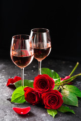 Two wine glasses of rose wine on brick background, bouquet of red roses for romantic evening for Valentines day surprise, marriage proposal passion and love celebration, copy space 