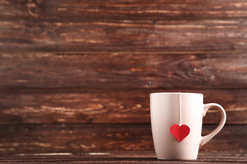 Cup with teabag and red heart on brown wooden table