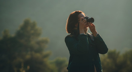 Long horizontal picture of tourist traveler photographer making pictures of green forest and nature, blured trees on the background, hipster girl looking on nature horizon, blank space for text
