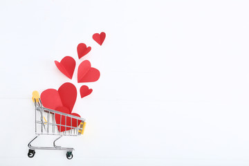 Shopping cart with paper hearts on white wooden table