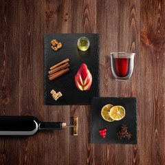 Mulled wine recipe ingredients and kitchen accessories, bottle of red wine, cinnamon, anise stars, orange, brown sugarand spice on rustic wood background.