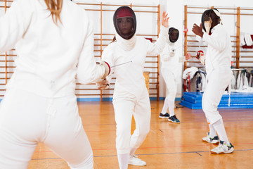 Two female fencers  exercising movements in duel at fencing room