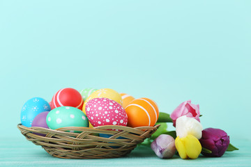 Colorful easter eggs in basket with tulips on wooden table