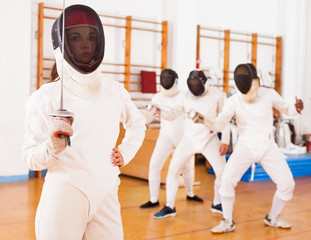 Young female in mask with foil at fencing workout