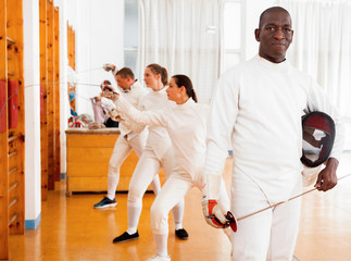 Active african american male fencer in uniform standing with mask and foil at fencing room