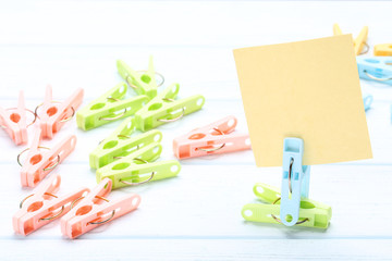 Colorful plastic clothespins with blank sheet of paper on wooden table