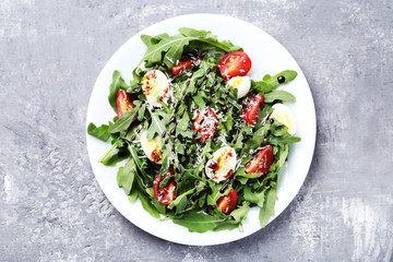 Salad with arugula leafs, tomatoes and eggs on grey wooden table