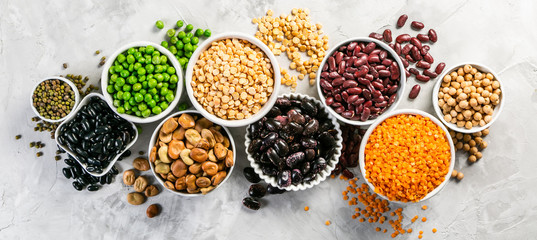 Selection of legumes - beans, lentils, mung, chickpea, pea in white bowls on stone background