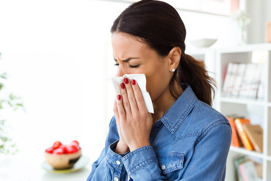 Unhealthy young woman sneezing in a tissue in the living room at home.