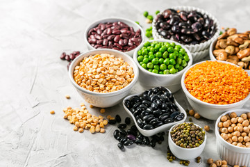 Selection of legumes - beans, lentils, mung, chickpea, pea in white bowls on stone background - obrazy, fototapety, plakaty
