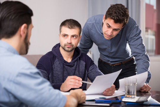 Three men worriedly discussing documents