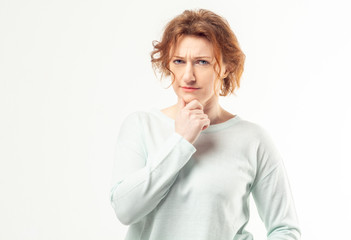 Beautiful red haired adult woman in casual looking into the camera with pensive expression, thinking or doubting about something on white background