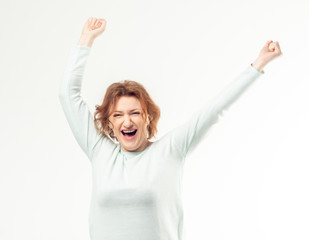 Beautiful happy excited red haired adult woman in casual with her hands in the air against white background