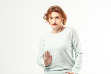 Beautiful red haired adult woman in casual looking into camera with frightened scared expression on her face, thinking about something, showing stop with her right hand on white background