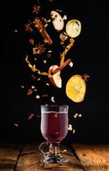 Glass of mulled wine with flying ingredients to prepare it on a black background
