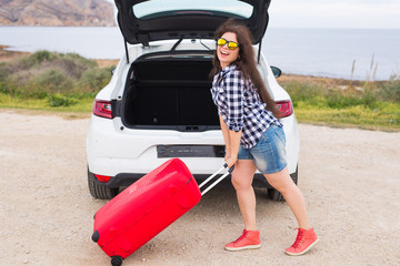Young woman standing near back of car smiling and getting ready to go. Summer road trip