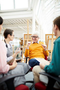 Portrait of joyful mature art teacher talking to group of students sitting in circle in art studio