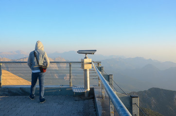 A young man watches sunrise in the mountains. Dawn in the mountains. Telescope on the observation deck on top of the mountain.