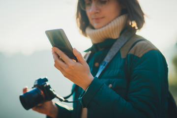 Close up image of pretty brunette girl using her mobile phone while doing photos of nature in the mountains, travelling around the world stays connected to internet, focus on cell telephone