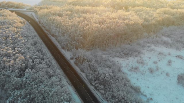 Magnificent winter landscape with forests covered with snow and a lonely road on a sunny morning. Wonderful sunset over the countryside. Aerial drone view.