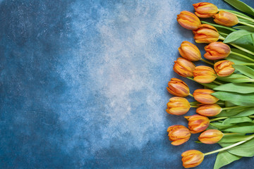 Orange tulips bouquet on blue watercolor background. Copy space, top view. Holiday background, greeting card